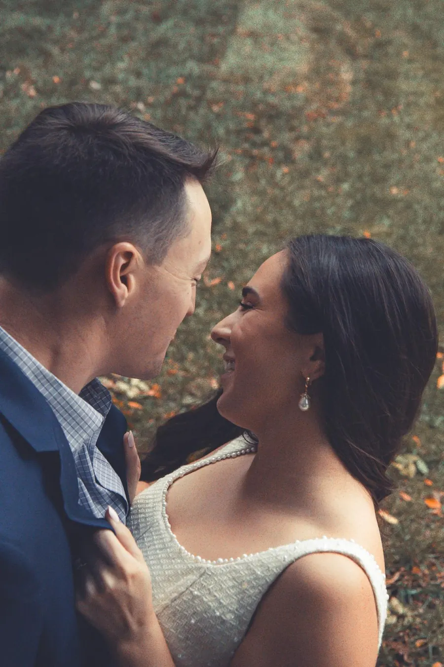 A bride and groom smiling at each other with fall color behind them