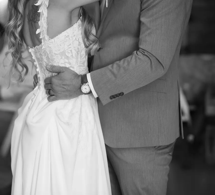 Black and white photo of a groom's arm around the bride's waist, her dress laced at the back