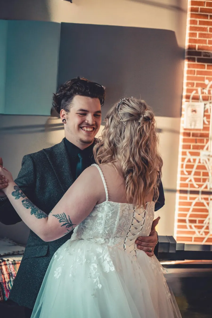 A couple dancing and laughing beside an exposed brick wall