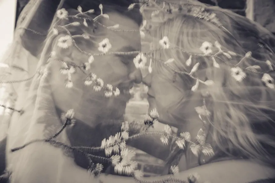 Black and white photo of a couple seen through a lace veil scattered with small flowers